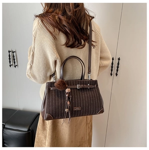 Detail of dark brown striped satchel showing matte texture and plush ball charm