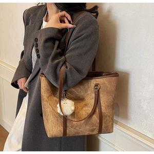 Detail of vintage brown leather tote bag with gold lettering and plush ball pendant