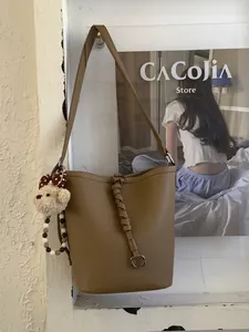 Brown leather bucket bag with braided rope detail and cute bear charm in life scene