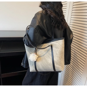 Detail shot of a large beige tote bag with black straps and plush white charm on the side