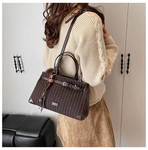 Detail of striped tote bag with brown leather trim and soft pom-pom keychain accessory