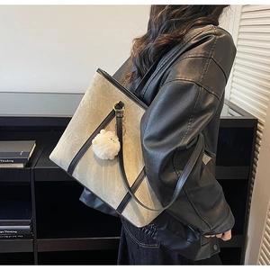 Detail of taupe suede tote bag with black straps and plush charm worn by model