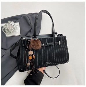 Detail of black striped tote bag featuring leather buckle and plush pompom charm
