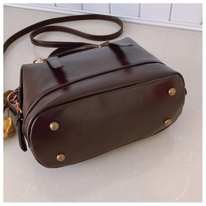 Details der braunen Boston-Tasche mit goldenen Standfüßen und kleinem Blumenanhänger