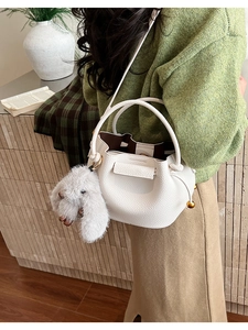 Close-up of white lychee-grain bucket bag with plush rabbit charm and elegant gold hardware