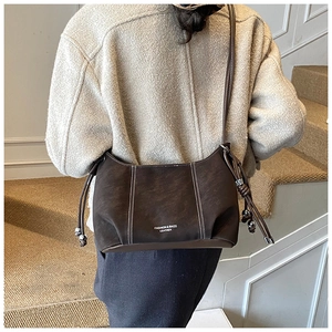 Detail of a dark brown leather half-moon crossbody bag with drawstring and metal beads