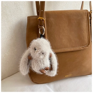 Détail d'un charme de lapin en peluche gris avec cuir marron sur un sac à bandoulière