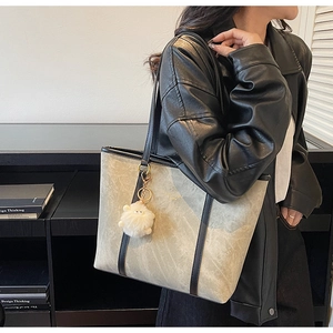 Detail of marble pattern tote bag with leather strap and plush sheep charm on a shoulder