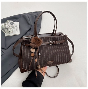 Detail of striped fabric and leather handbag with a decorative tassel and buckle strap