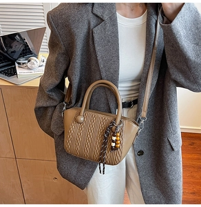 Detailed view of woven texture and wooden bead charm on caramel brown crossbody bucket bag