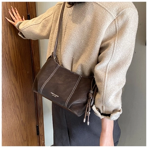 Detail of dark brown leather handbag with contrast stitching and drawstring tassel accessory