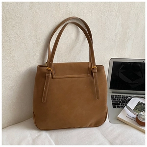Détail d'un cabas en daim marron avec fines lanières et boucle en métal sur un bureau