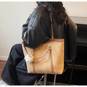 Detail of beige textured tote bag with brown leather trim and white pom-pom charm decoration