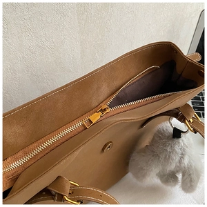 Détail du sac cabas marron caramel avec fermeture zippée et pompon gris décoratif