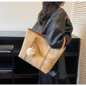 Detail of light khaki tote bag with dark brown straps and white pom-pom on model