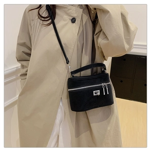 Détail d'un sac bandoulière vintage noir avec fermeture argentée sur un manteau beige