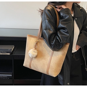 Detail of khaki tote bag with vintage texture and white pompom charm on a model
