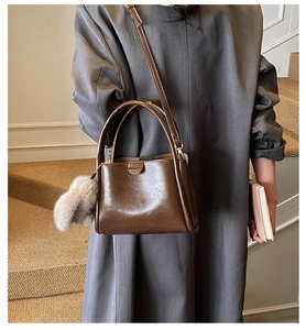 Detail of dark brown leather handbag with a plush grey faux fur pompom keychain