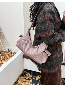 Detail of a dusty pink pleated leather shoulder bag worn over a plaid coat in autumn