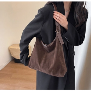 Detail view of dark brown suede hobo bag with brand tag on model in black blazer