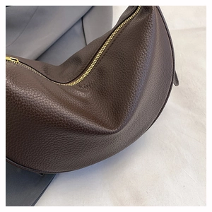 Detail of dark brown lychee grain leather texture and golden zipper on crossbody bag
