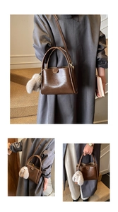 Detail of a brown leather bucket bag with top handles and a soft faux fur charm