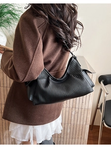 Detail of black pleated shoulder bag showing vertical texture and crescent shape on model