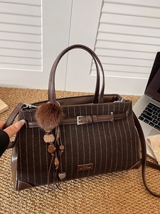 Brown striped corduroy tote bag with plush tassel charm shown in a home office setting