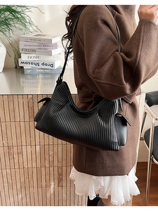 Detail of black pleated faux leather shoulder bag with decorative buckle on side