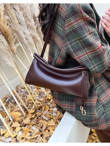 Dettaglio macro della borsa baguette in pelle marrone scuro con bordi tubolari e ciondolo