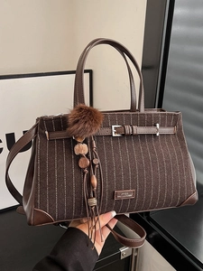 Brown striped tote bag with plush charm and handle shown in a commuter lifestyle setting