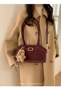 Detail of burgundy retro handbag with gold buckle and plush bear charm on beige coat