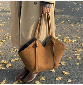 Detail of brown suede tote bag with V-cut opening and knotted handle design on street