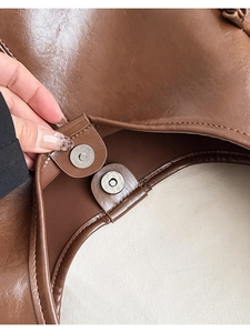 Close-up of magnetic snap closure on brown oil wax leather shoulder bag with fine stitching