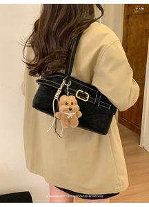 Detail of black suede shoulder bag with contrast stitching and a teddy bear charm