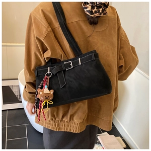 Détail d'un sac à bandoulière en suédine noire avec boucles et un joli pendentif d'ours