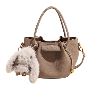 Detail of taupe pleated bucket bag with lychee texture and cute plush rabbit charm
