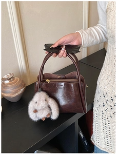 Detail of dark brown oil wax leather handbag with plush rabbit pendant and logo