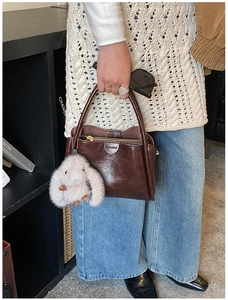 Detail of dark brown leather handbag with gold zipper and plush rabbit charm accessory