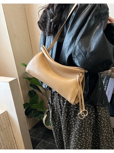 Dettaglio borsa baguette plissettata beige con fibbia metallica su giacca di pelle