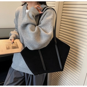 Detail of a large black faux suede tote bag featuring a unique hexagonal cut and metal feet