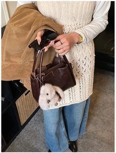 Detail of dark brown leather tote bag with plush animal charm and zip closure