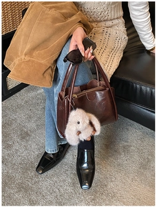 Detailed close-up of brown vintage leather handbag with a plush bunny charm on a model