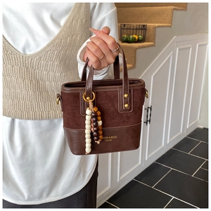 Close-up of brown bucket bag with suede patchwork, gold hardware, and beaded charm