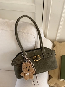 Olive green vintage shoulder bag with golden buckle and plush dog charm on white sofa