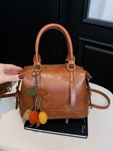 Vintage braune Boston Handtasche mit Deko-Anhängern und Trageriemen auf Büchern präsentiert