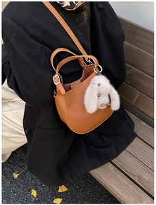 Brown lychee leather bucket bag with a cute white plush rabbit charm on a park bench