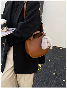 Brown lychee leather crescent bag with cute plush bunny charm and golden autumn leaf background
