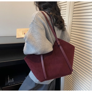 Detail of burgundy suede tote bag with leather straps worn by model in lifestyle setting