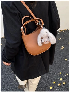 Brown lychee leather crescent bucket bag with rabbit charm on a street with ginkgo leaves